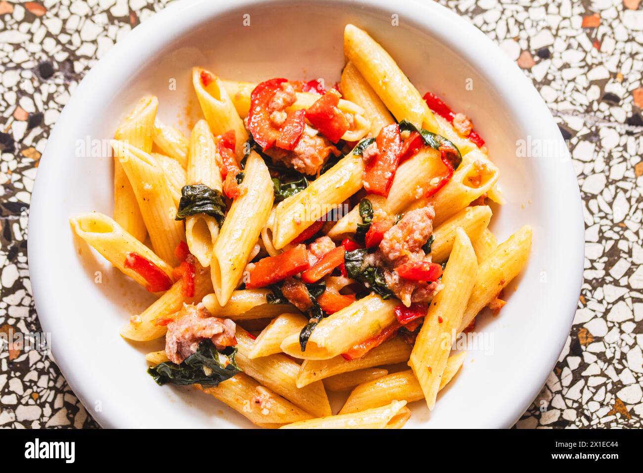 Penne avec salsiccia salée, tomates juteuses et feuilles tendres d'épinards Banque D'Images