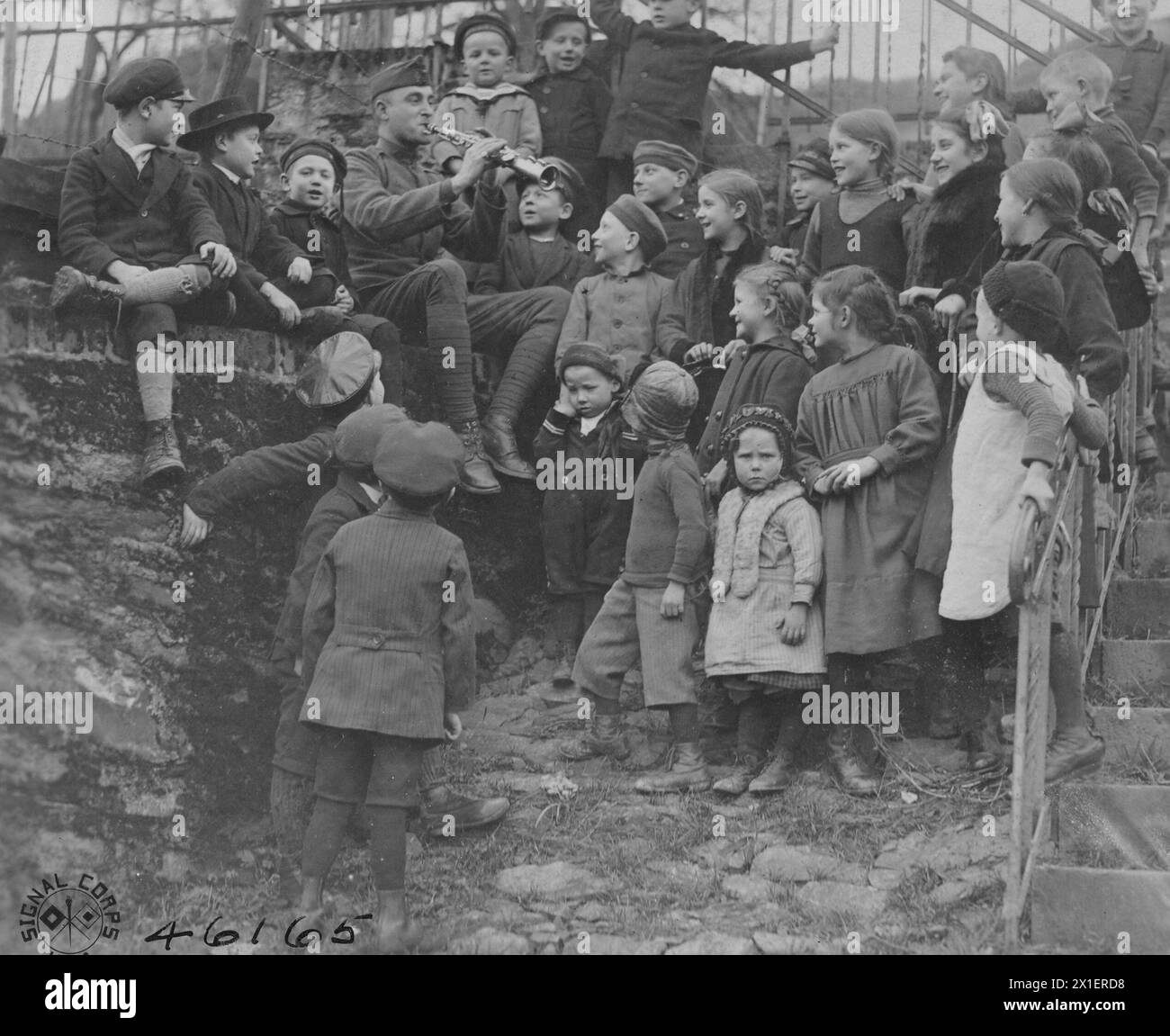 MUSICIEN JOE FOSTER DU 51st Infantry Band, 4th Army corps, enseignant des chansons américaines aux enfants allemands. Il est assis sur un mur dans l'une des rues du village et les enfants sont regroupés autour de lui chantant. Cochem, Allemagne CA. 1919 Banque D'Images