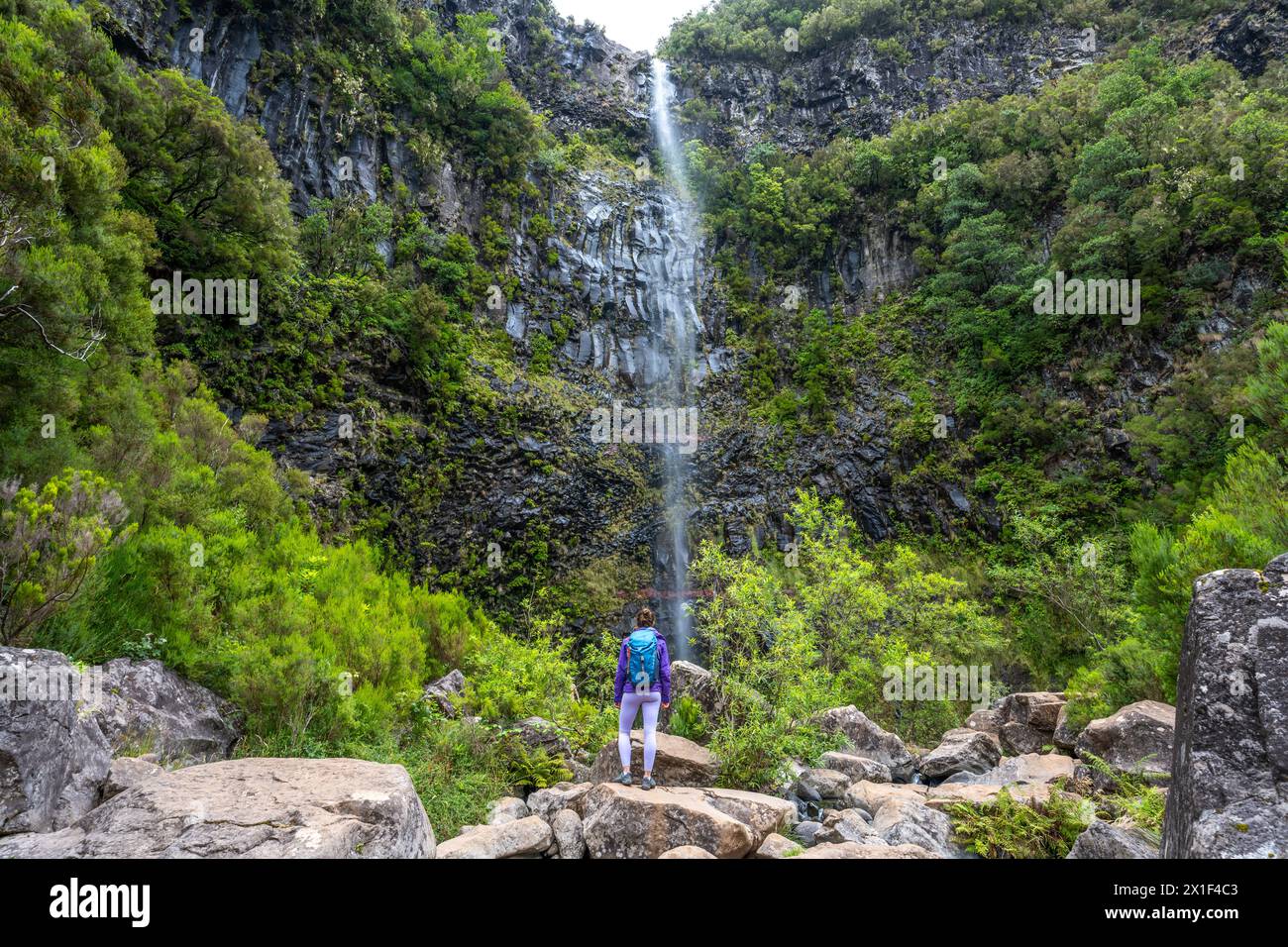 Description : femme touriste avec sac à dos profite de l'atmosphère à la chute d'eau tombant de haut mur de roche. Cascade de Lagoa do Vento, île de Madère, Portug Banque D'Images