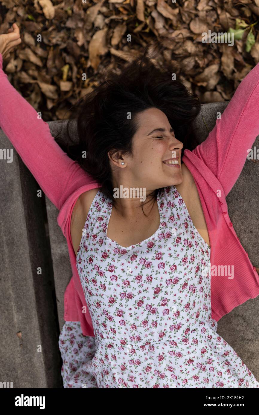 La jeune femme latino-américaine (33 ans) avec une attitude positive est très heureuse de l'arrivée du printemps. Elle est allongée sur le dos, fond de feuilles sèches. SH Banque D'Images