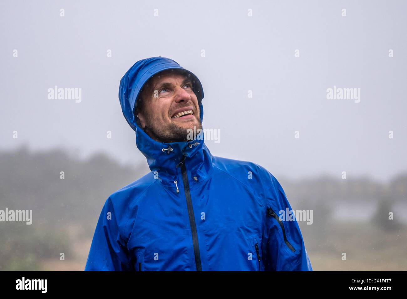 Description : touriste masculin heureux et en bonne santé regardant dans le ciel tout en souriant et en profitant d'un mode de vie actif dans la nature et en plein air sous la pluie. 25 Fontes Banque D'Images