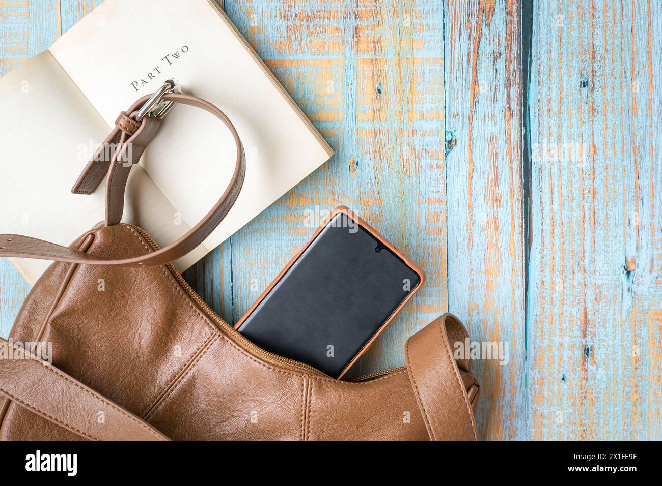 Sac à main femme en cuir de couleur marron avec téléphone et livre de poche. Vue de dessus, espace de copie. Banque D'Images