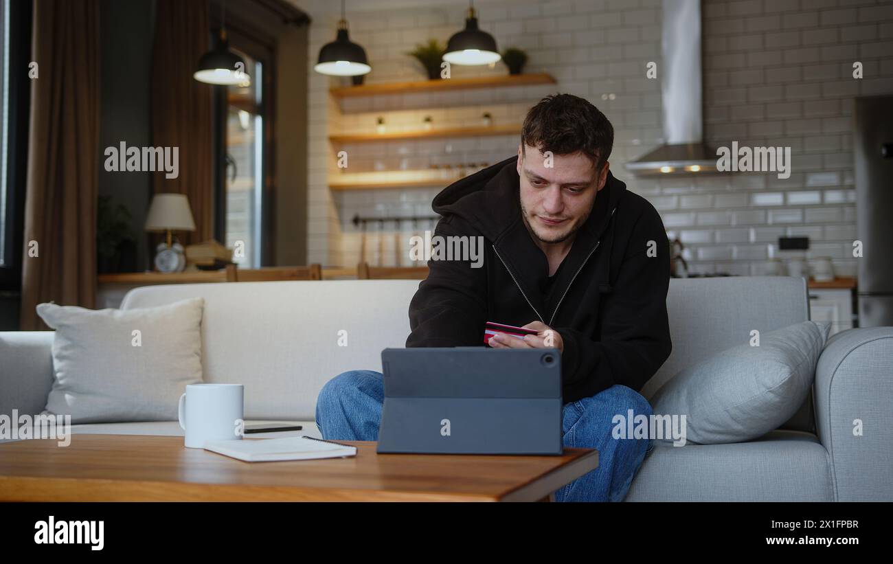 Homme assis sur le canapé à la maison entrant le numéro de carte de crédit sur la tablette pour la boutique en ligne carte de crédit est refusé ou hors limite, se sentir en colère et unha Banque D'Images