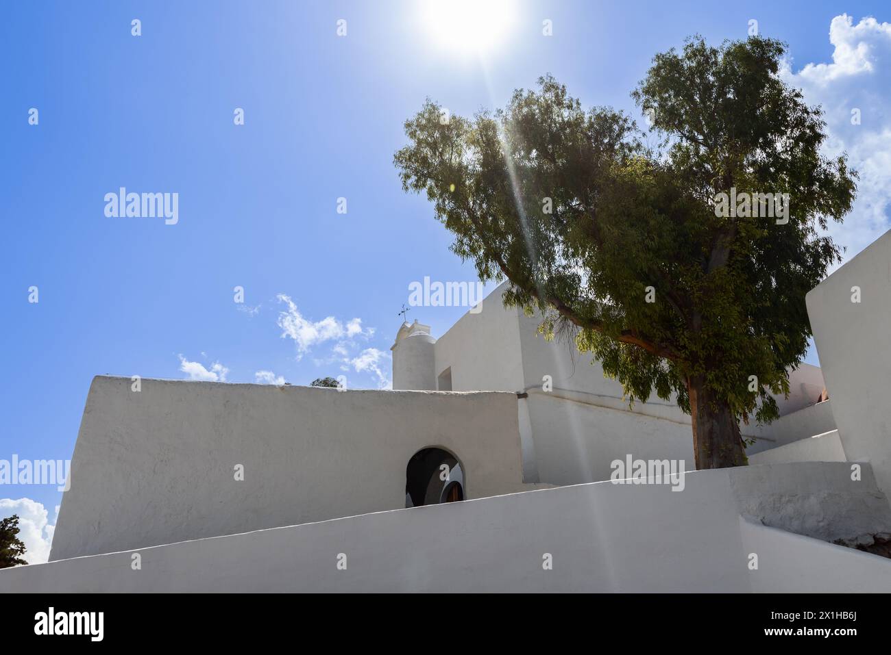 Église Puig de Missa à Santa Eulalia, Ibiza, avec des rayons du soleil perçant le feuillage d'un arbre adjacent, complétant l'architecture blanche et dure Banque D'Images