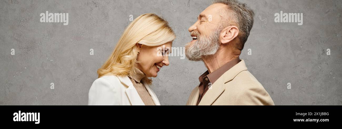 Un couple aimant élégant et mature dans des vêtements debonair pose ensemble sur un fond gris. Banque D'Images