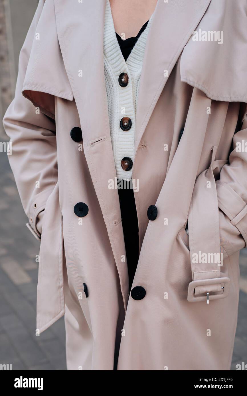 Détails de fantaisie Street style d'un pull boutonné blanc tricoté et trench beige pour femme avec ceinture. Mode urbaine contemporaine Banque D'Images
