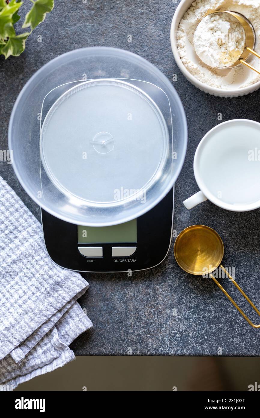 Balances, cuillère à mesurer, serviette, eau et farine sur le comptoir de cuisine en béton Banque D'Images