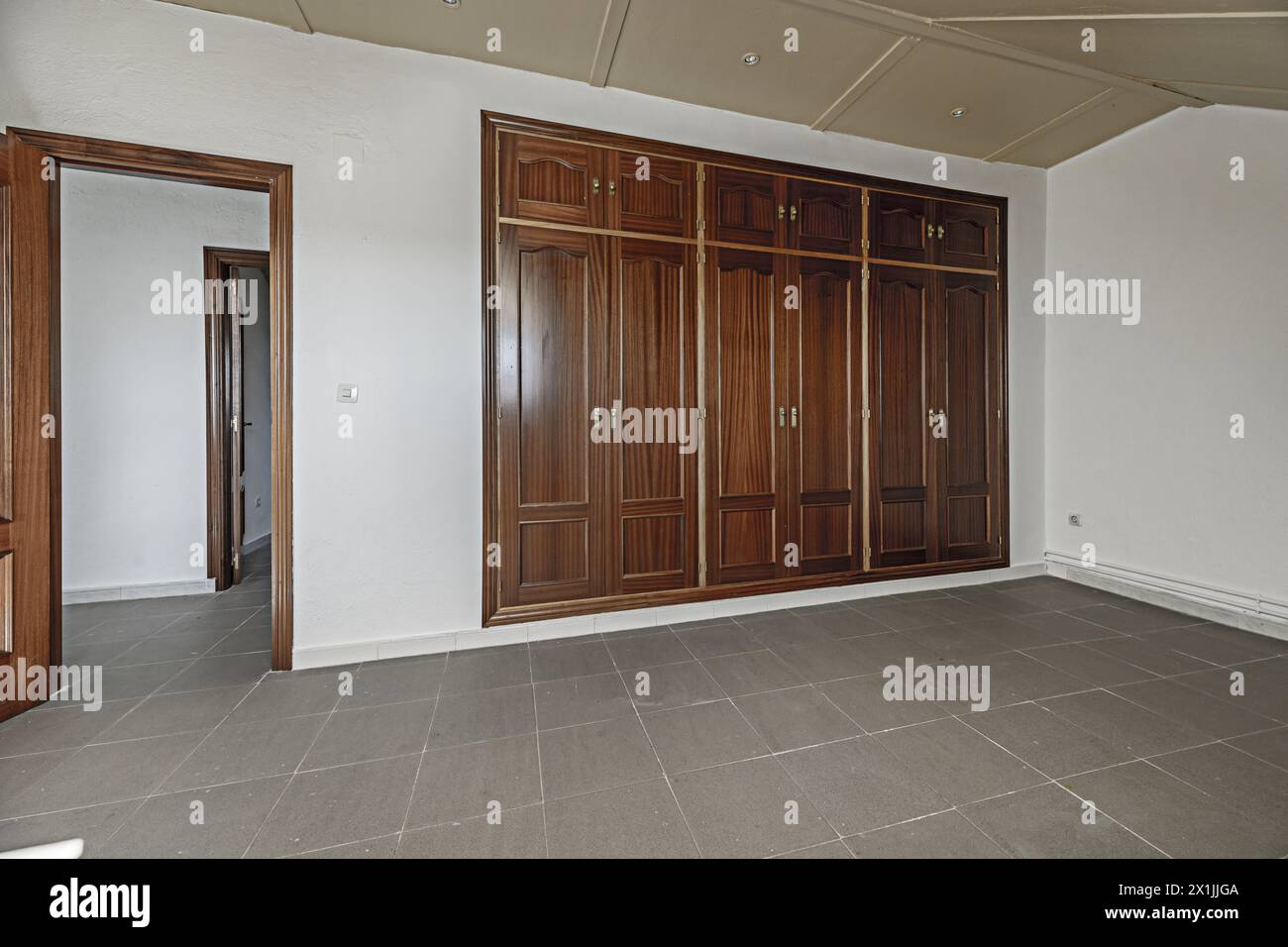 Grande chambre dans une pièce mansardée avec une grande armoire intégrée couvrant un mur et sols en grès gris sale Banque D'Images