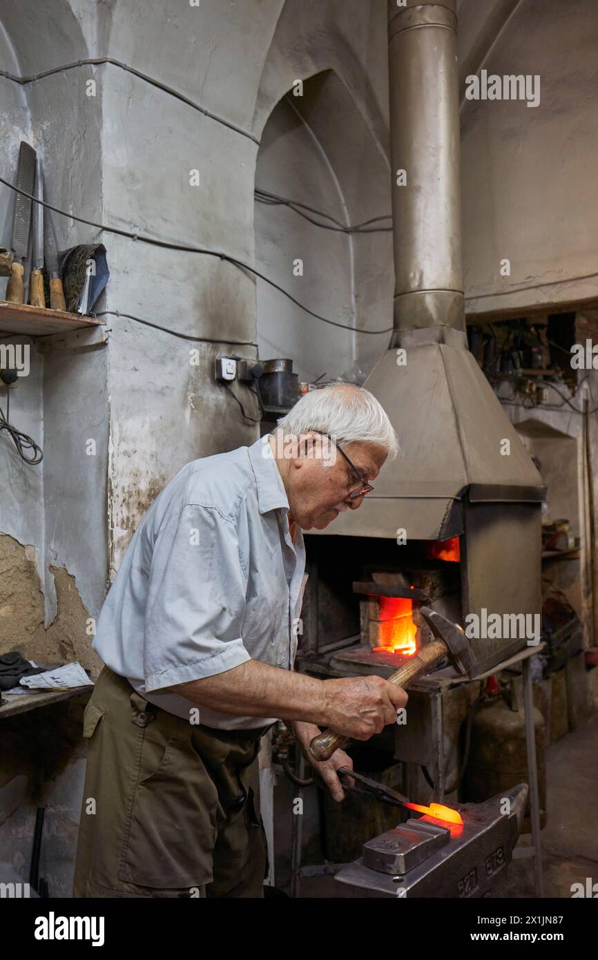 Un forgeron iranien forge une billette rouge avec un marteau dans son forgeron. Ispahan, Iran. Banque D'Images