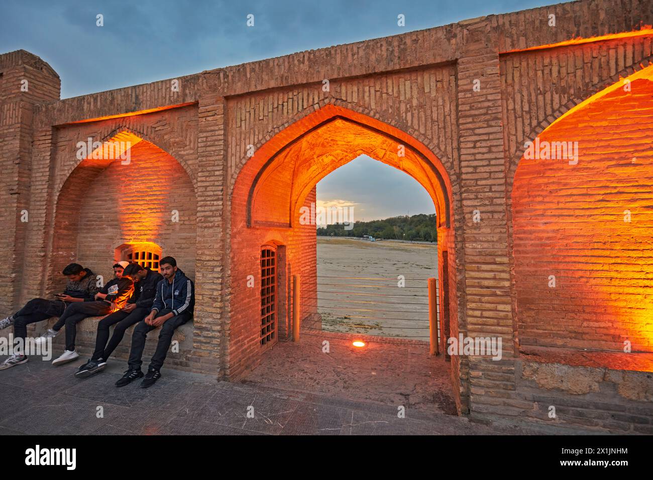 De jeunes Iraniens sont assis sur le pont Allahverdi Khan, alias si-o-se-pol (XVIIe siècle), illuminé au crépuscule. Ispahan, Iran. Banque D'Images