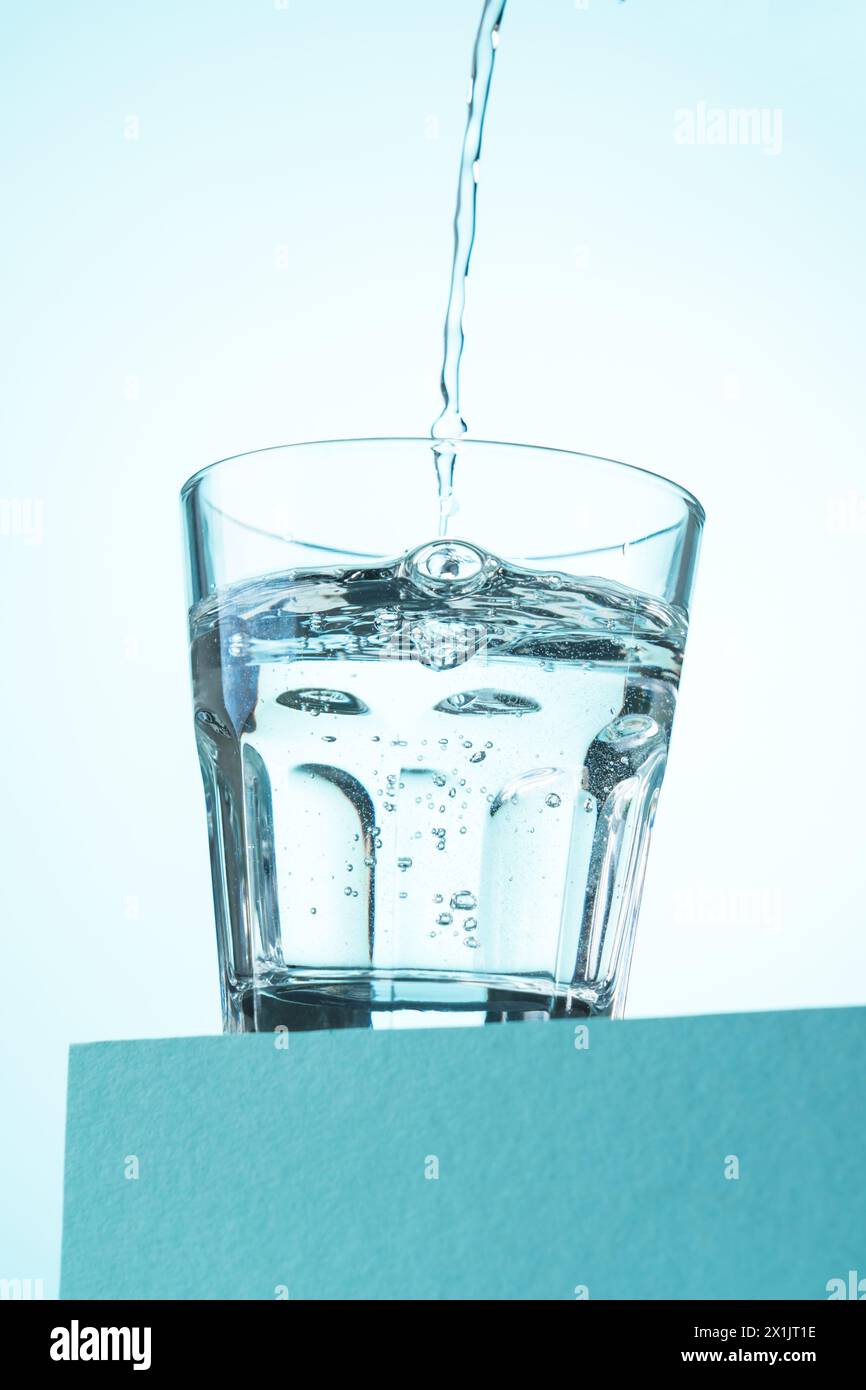 Verser de l'eau dans le verre sur bleu. Banque D'Images