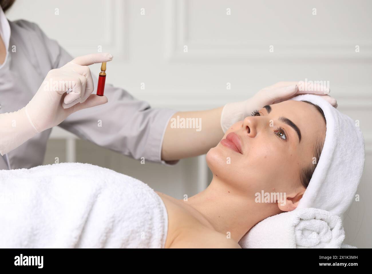 Cosmétologue professionnel tenant l'ampoule de soins de la peau tout en travaillant avec le client en clinique, gros plan Banque D'Images