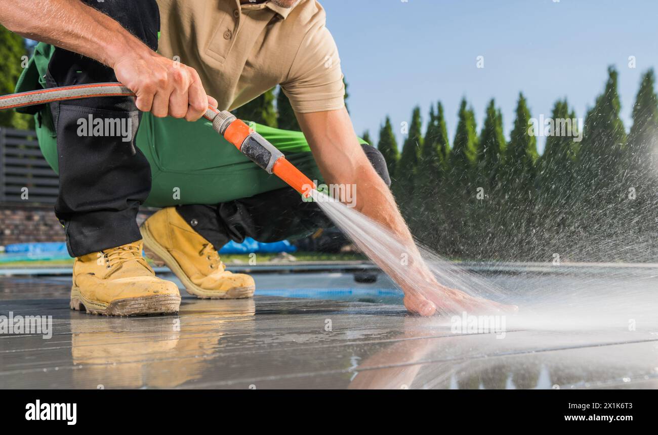 Propriétaire composite Deck lavage au bord de la piscine à l'aide du tuyau d'arrosage Banque D'Images