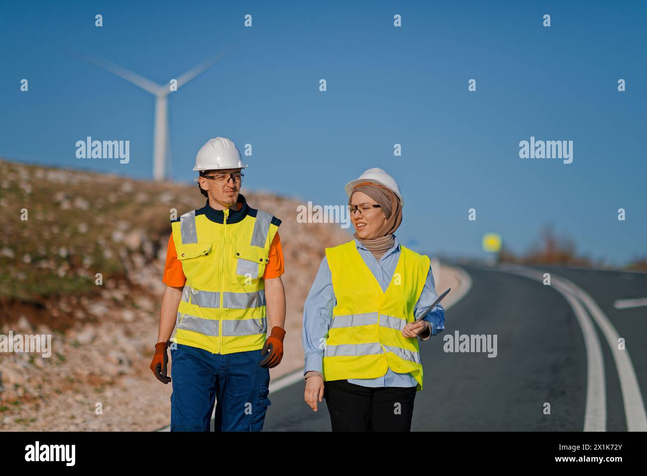 Une ingénieure avec une tablette et son collègue inspectent les éoliennes dans un champ, démontrant le travail d’équipe et le dévouement aux projets d’énergie renouvelable Banque D'Images