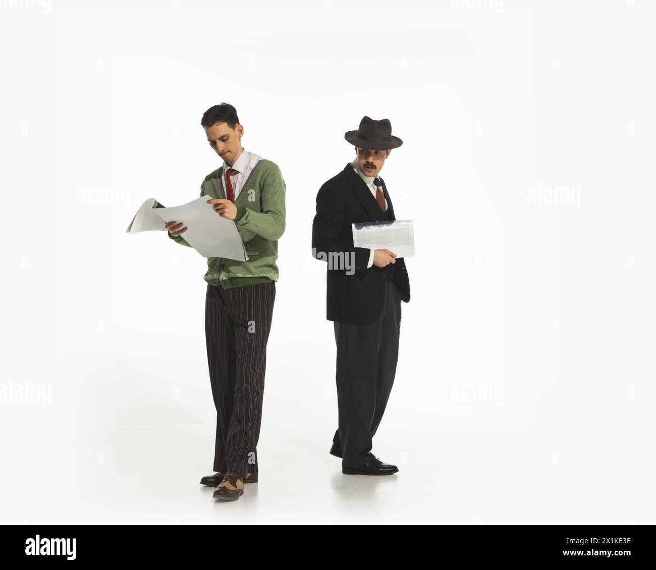 Deux hommes dans des vêtements de style rétro avec des journaux isolés sur fond blanc. Homme regardant avec intérêt caché sur les papiers Banque D'Images