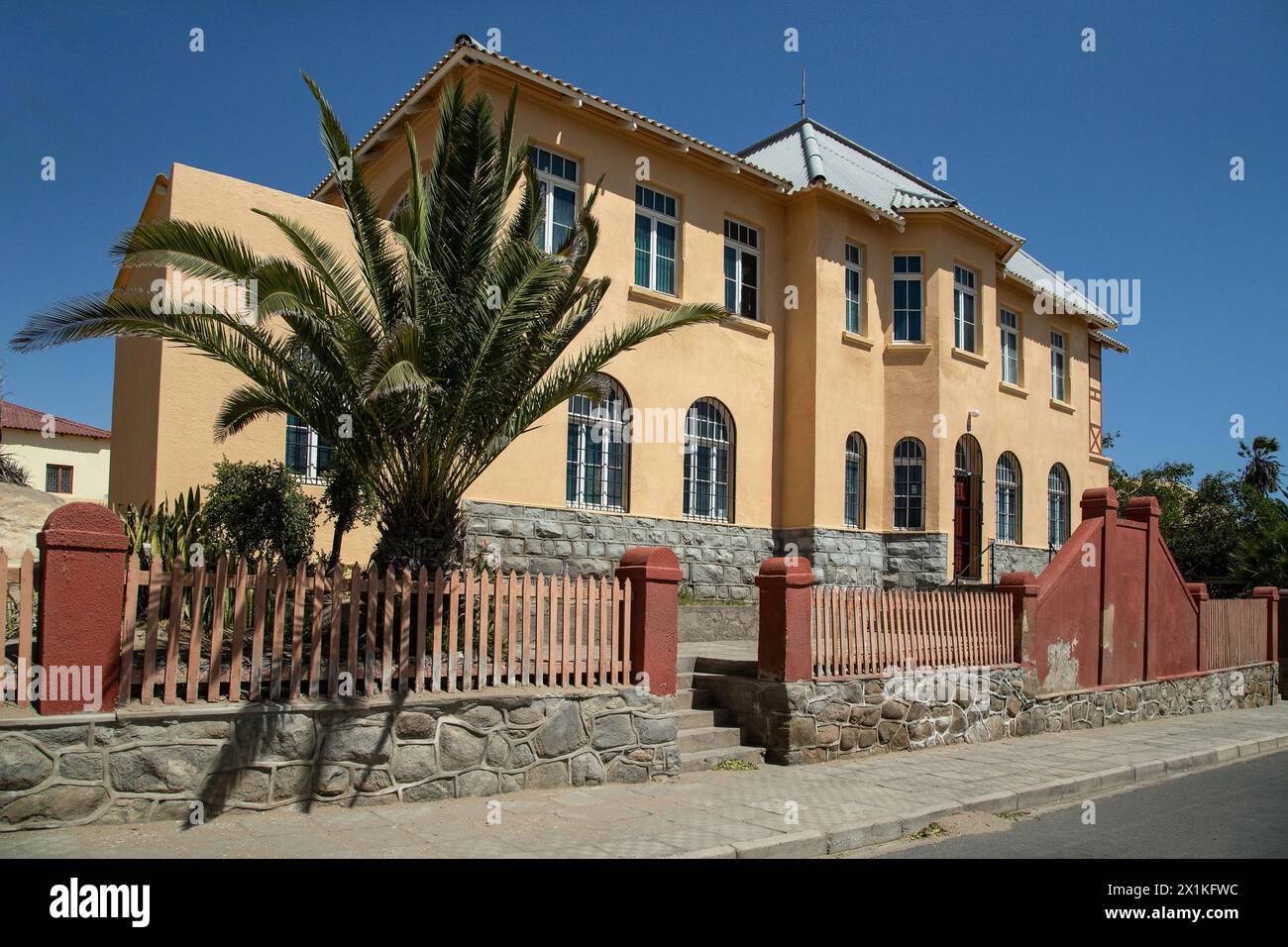 Historique, crème, maison coloniale allemande avec détails en terre cuite, clôture, palmier et marches jusqu'à la porte à Luderitz, Namibie. Banque D'Images