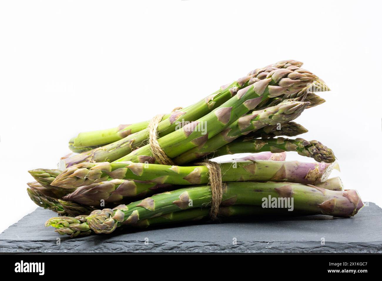 Gros plan de faisceaux d'asperges crues fraîches sur une ardoise isolée sur un fond blanc Banque D'Images