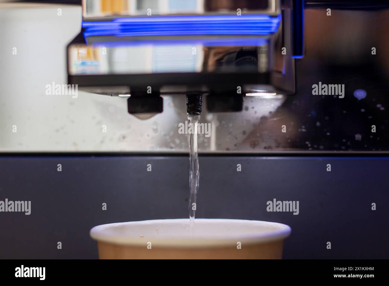 Une tasse bleue de café liquide est versée d'une machine dans un verre, créant une solution fluide pour une boisson rafraîchissante Banque D'Images