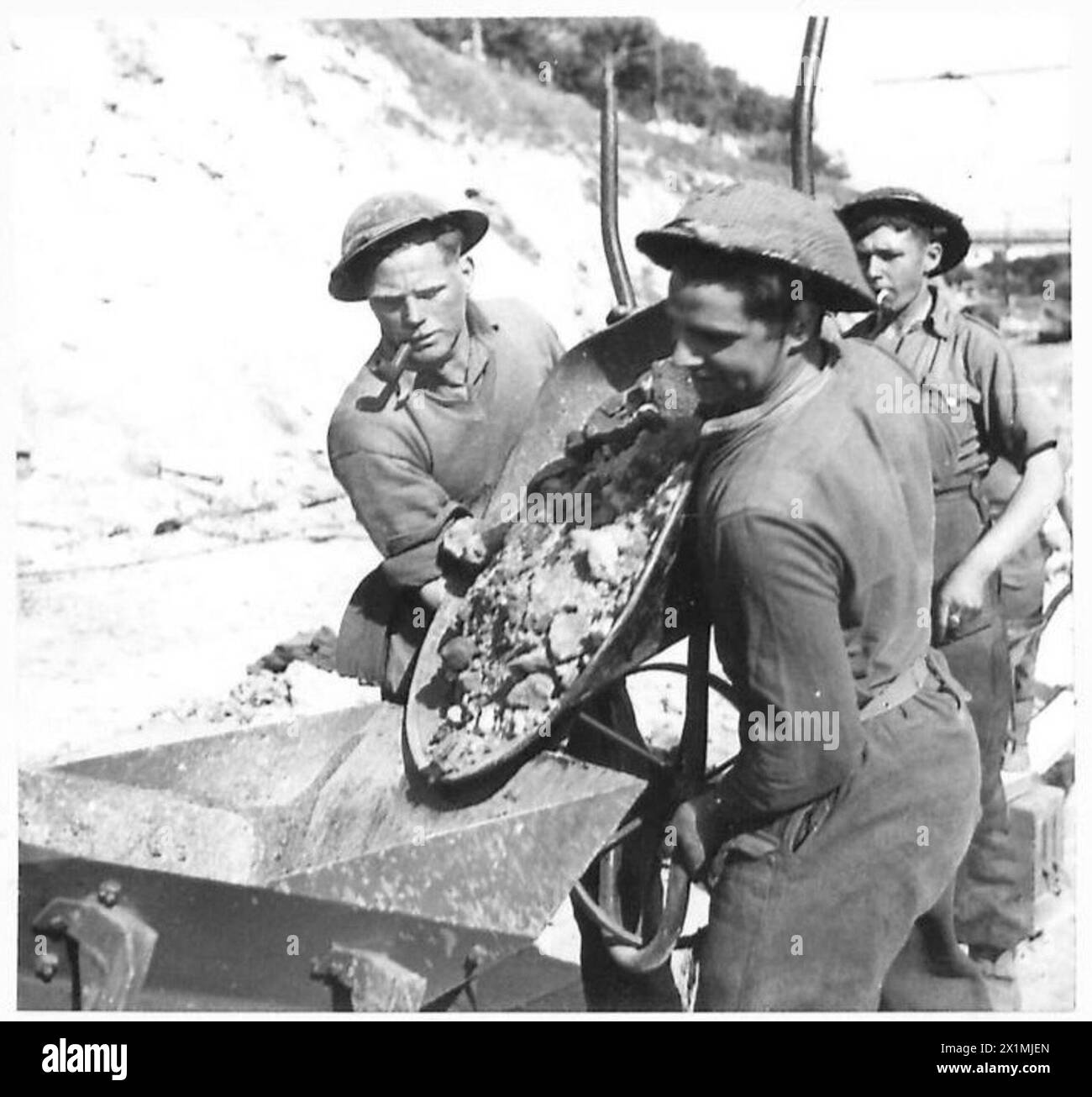 SPR MacDonald et l/Cpl. N. Doig de l'armée britannique fait basculer une brouette de pierres dans un concasseur, illustrant le travail manuel et le travail de construction pendant les campagnes en Afrique du Nord, en Sicile, en Italie, dans les Balkans et en Autriche. Banque D'Images