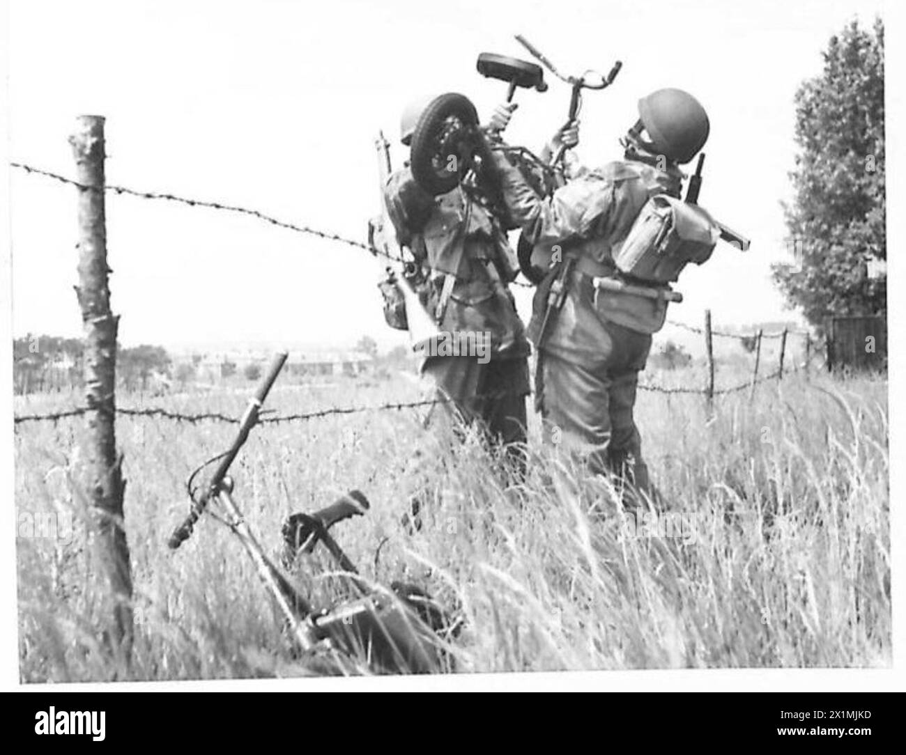 Les troupes de parachute manœuvrent un scooter Welbike sur une clôture de fil barbelé, démontrant la portabilité de ce petit véhicule militaire sous les opérations de l'armée britannique. Banque D'Images