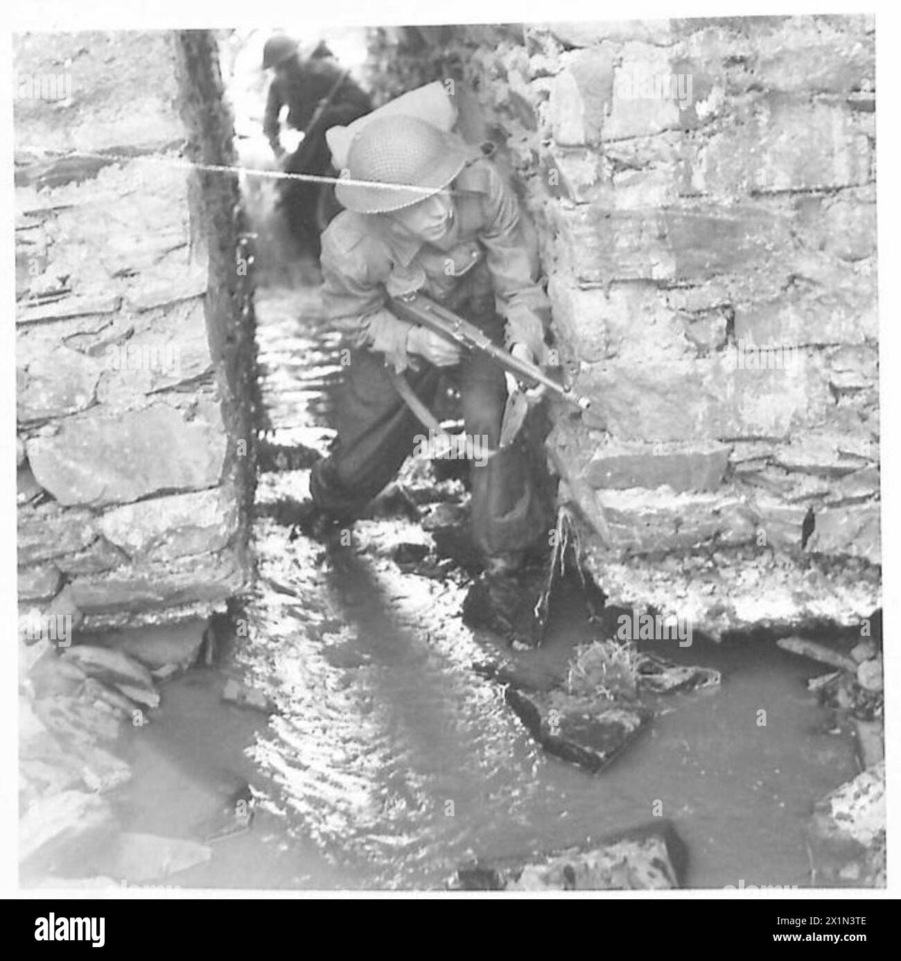 Un soldat avance prudemment à travers un ponceau avec son canon Tommy lors de l'entraînement à l'école de bataille de l'armée britannique. Banque D'Images
