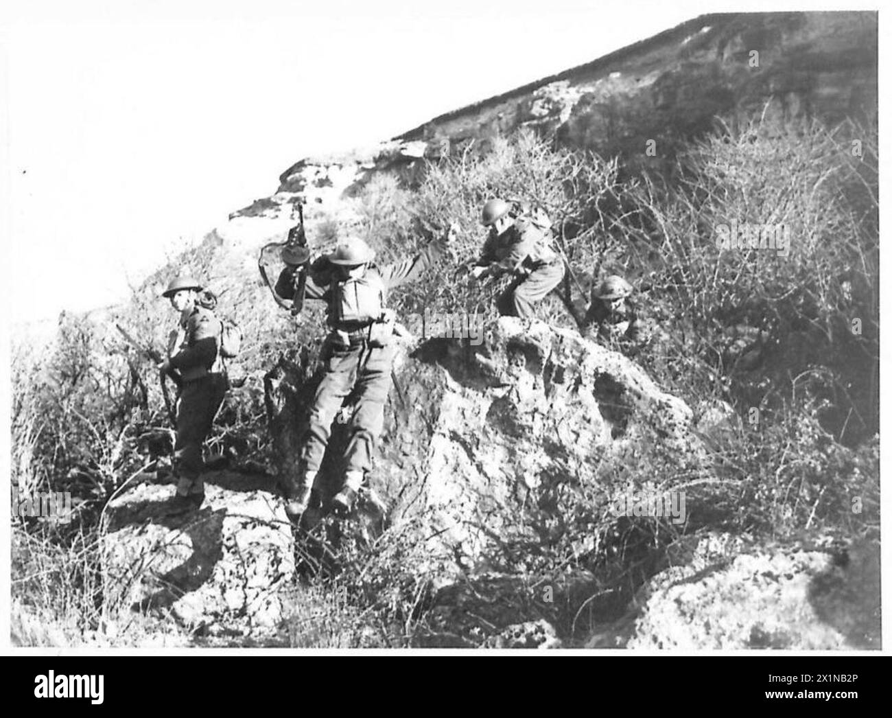 Les soldats du Suffolk Regiment manœuvrent à travers les buissons et grimpent sur les rochers pendant les opérations d'entraînement de l'armée britannique. Banque D'Images