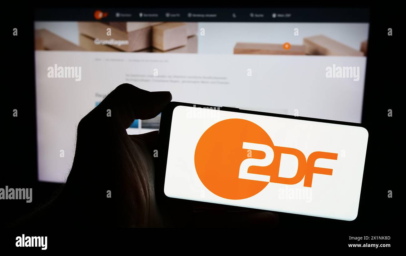 Personne tenant le téléphone portable avec le logo de la chaîne de télévision Zweites Deutsches Fernsehen (ZDF) en face de la page Web. Concentrez-vous sur l'affichage du téléphone. Banque D'Images