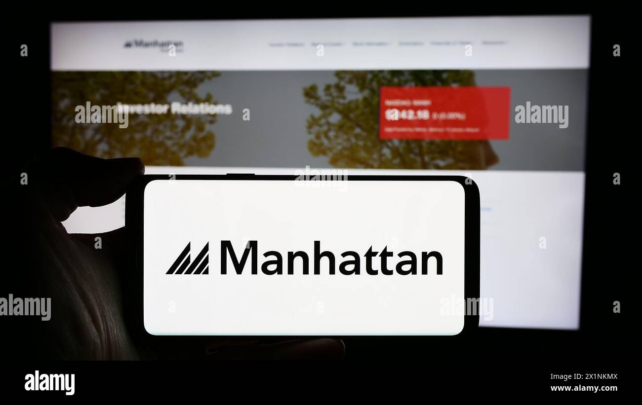 Personne tenant le téléphone portable avec le logo de la société américaine de logiciels Manhattan Associates Inc devant la page Web de l'entreprise. Concentrez-vous sur l'affichage du téléphone. Banque D'Images