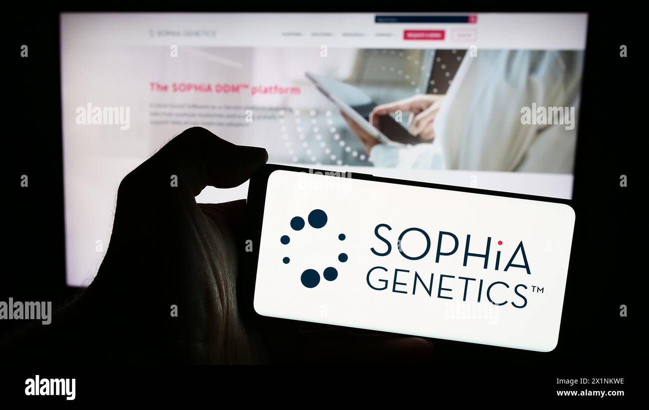 Personne tenant un smartphone avec le logo de la société suisse de logiciels de santé Sophia Genetics sa en face du site. Concentrez-vous sur l'affichage du téléphone. Banque D'Images