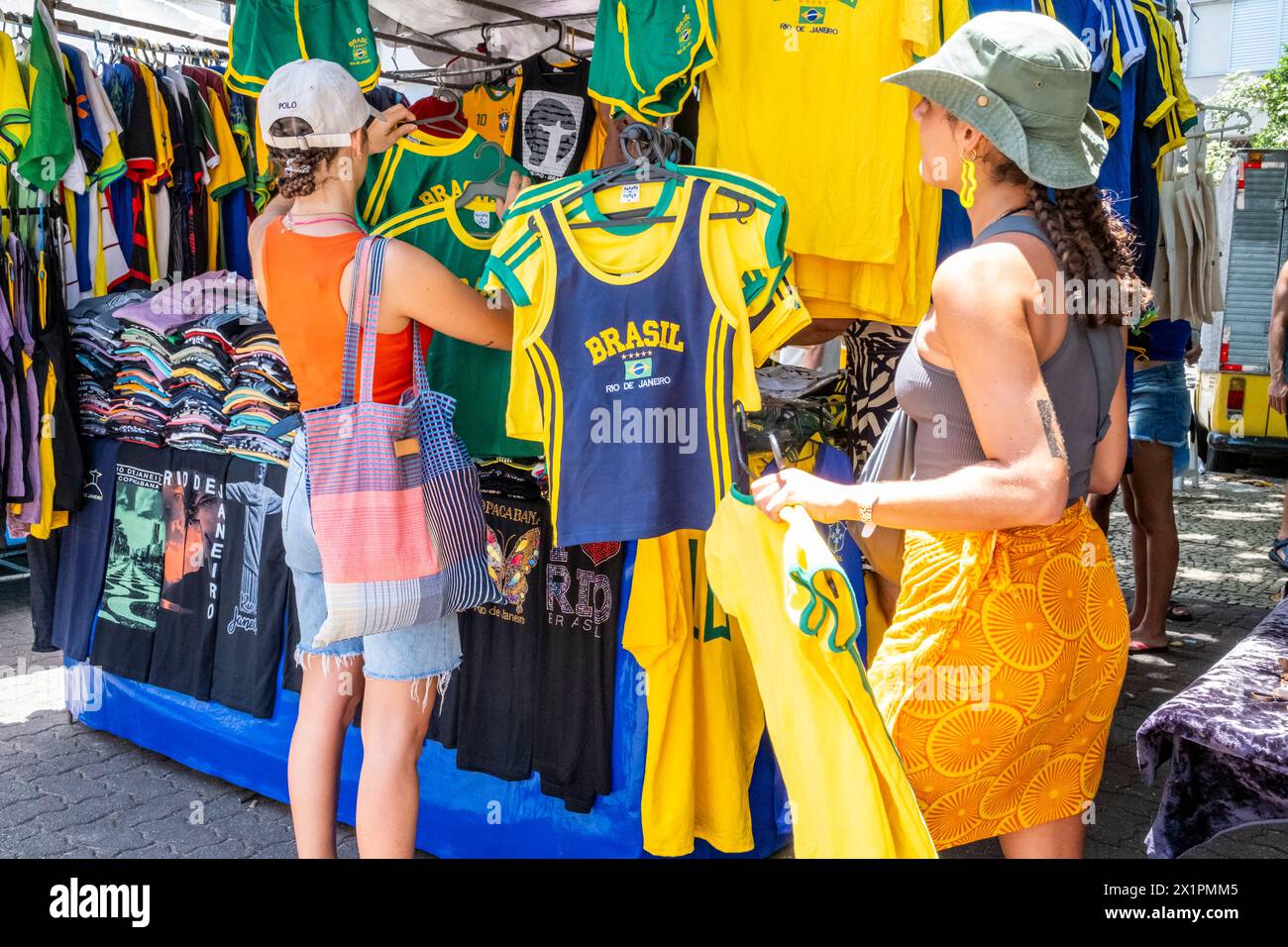 Deux jeunes femmes choisissent des maillots de football brésiliens au marché du dimanche d'Ipanema (foire hippie), Rio de Janeiro, État de Rio de Janeiro, Brésil. Banque D'Images