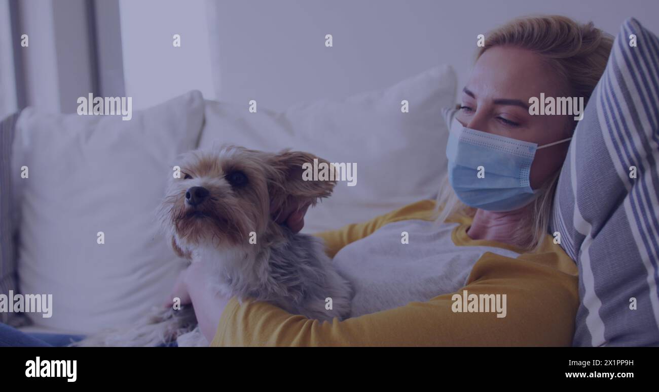 Femme caucasienne portant un masque câlin avec un chien sur un canapé Banque D'Images