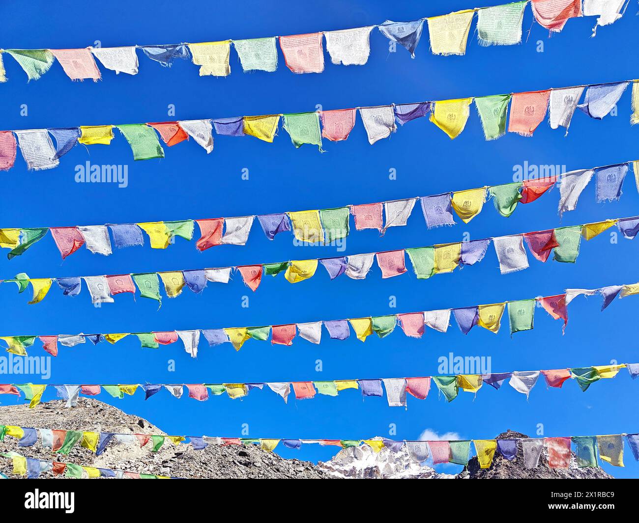 Des drapeaux de prière tibétains flottent contre un ciel bleu clair, haut dans l'Himalaya. Banque D'Images