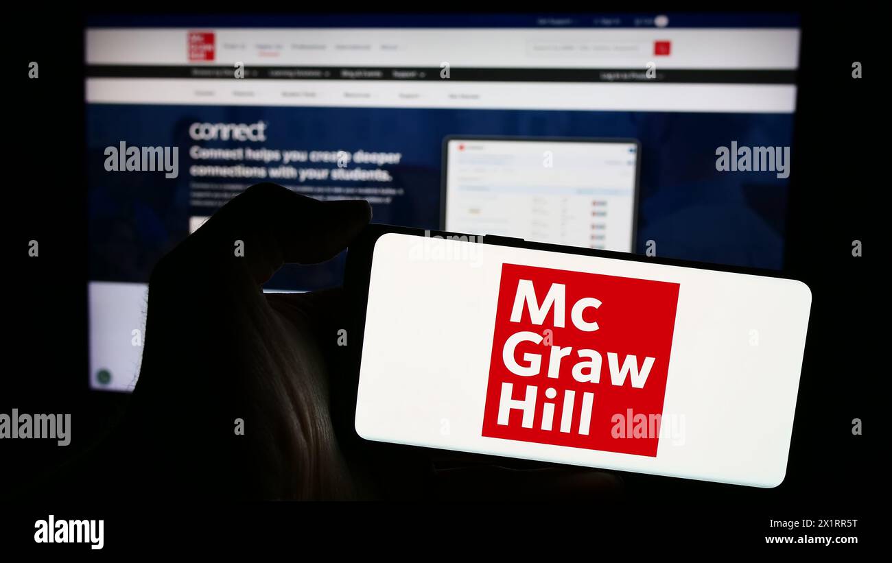 Personne tenant le téléphone portable avec le logo de la société d'édition américaine McGraw Hill LLC en face de la page Web d'affaires. Concentrez-vous sur l'affichage du téléphone. Banque D'Images