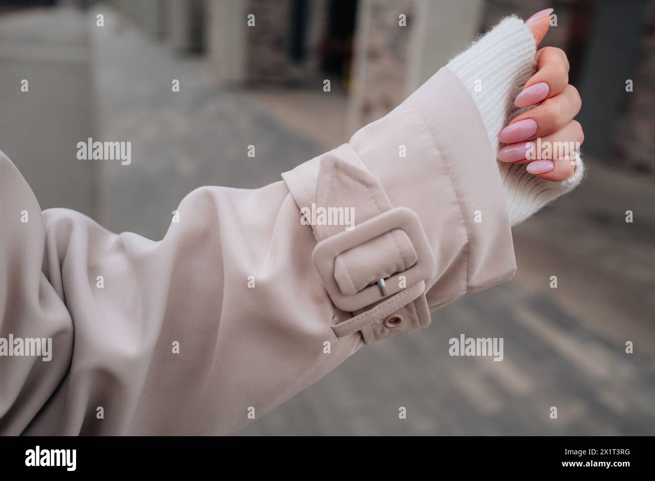 Détails de mode d'une manche de trench femme beige, main féminine avec manucure rose Banque D'Images
