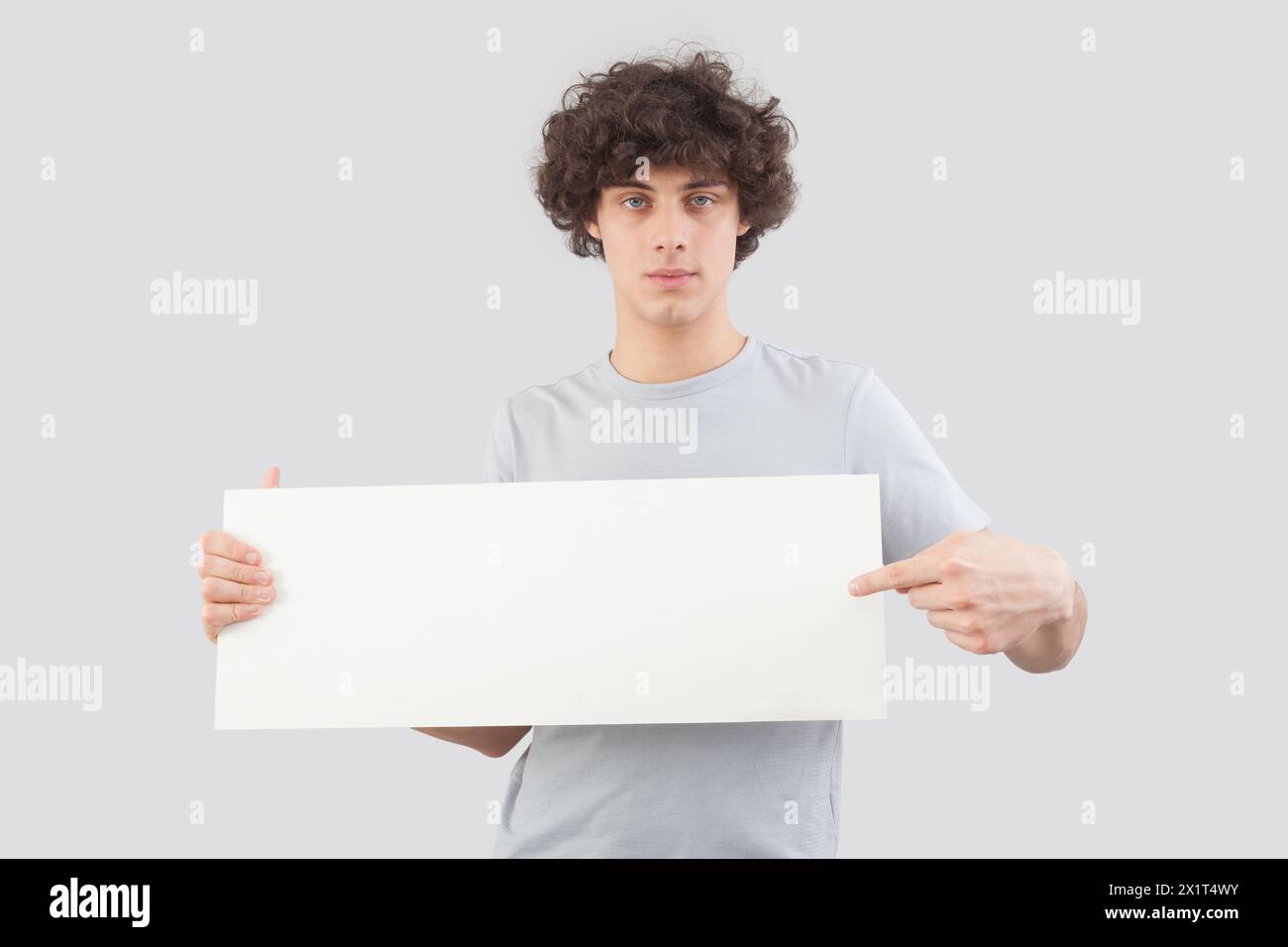 Beau jeune homme, pointant avec le doigt pour montrer un panneau blanc vierge, isolé sur fond gris. Espace de copie de placard pour le texte ou le logo, bannière pour Banque D'Images