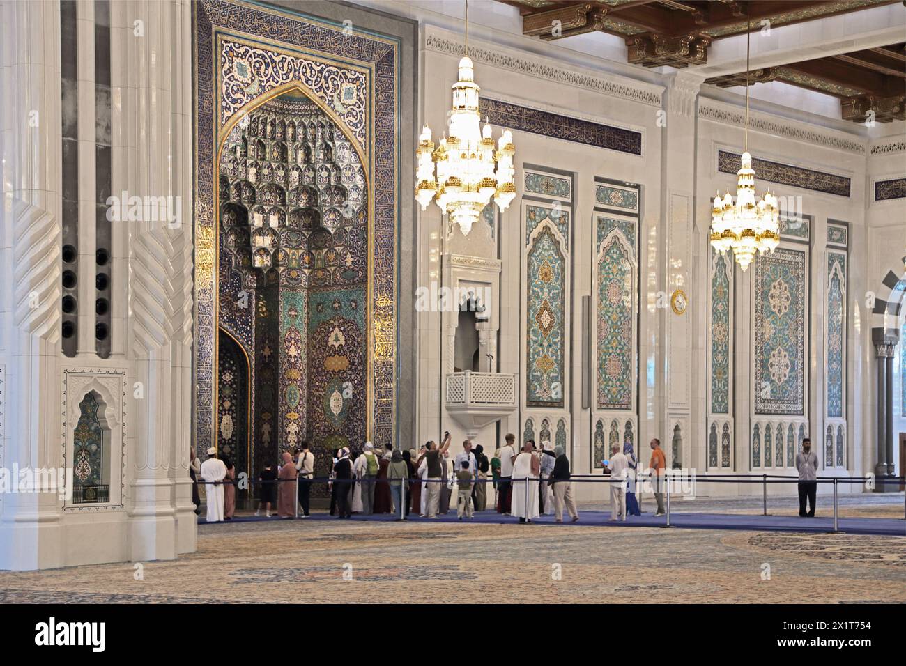 Sultan Qaboos Grand Mosquée touristes intérieurs debout sur le tapis bleu protecteur par le mihrab Muscat Oman Banque D'Images