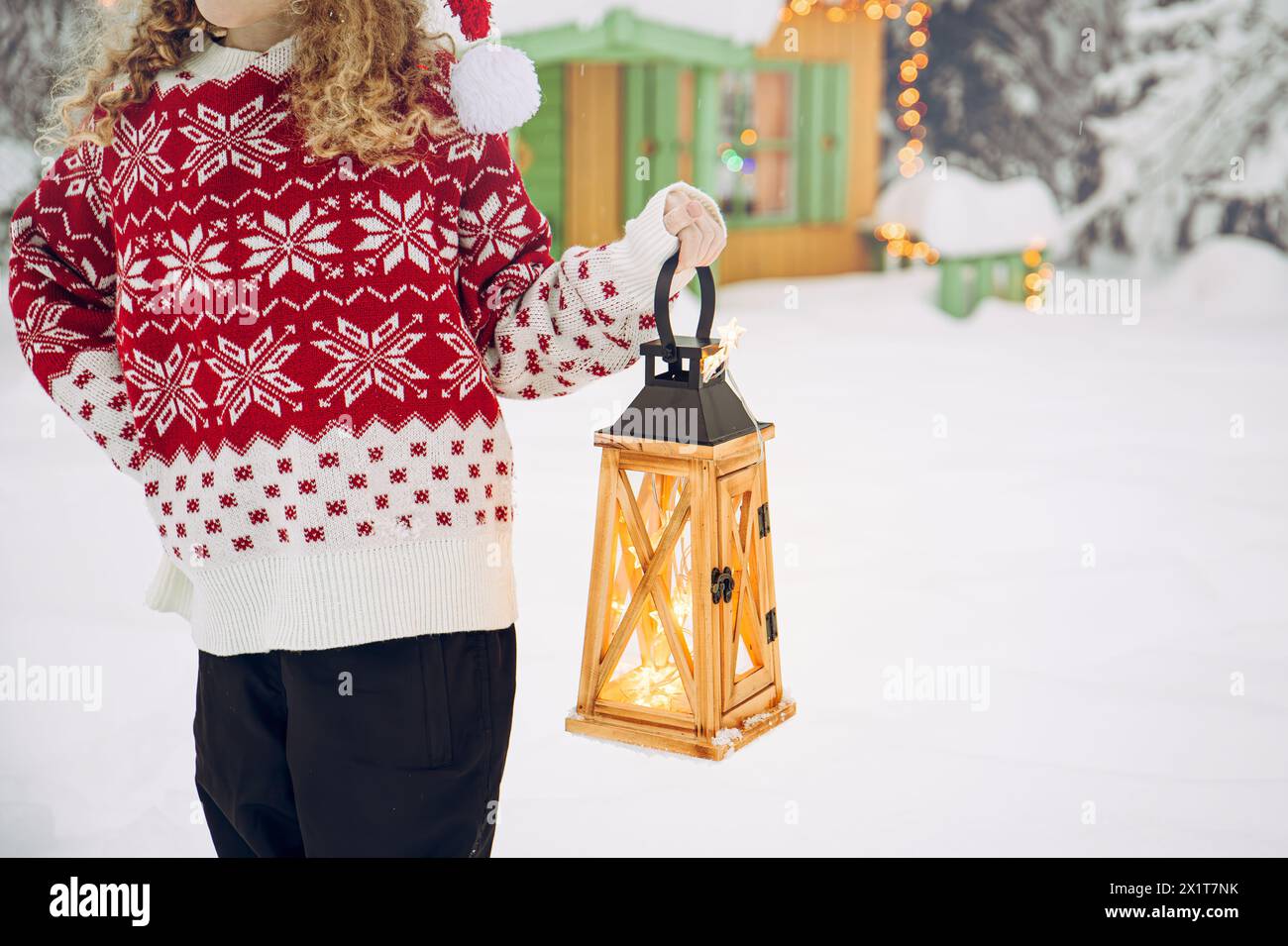 Vue rapprochée de la main de l'enfant tenant la lanterne en bois et portant le pull traditionnel de Noël à motif à l'extérieur en hiver neigeux. Banque D'Images