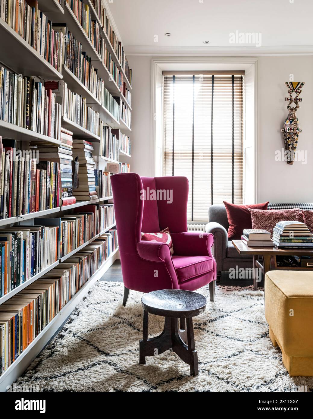 Fauteuil wingback rembourré rose avec étagères de livres dans la maison Chelsea, Londres, Royaume-Uni Banque D'Images