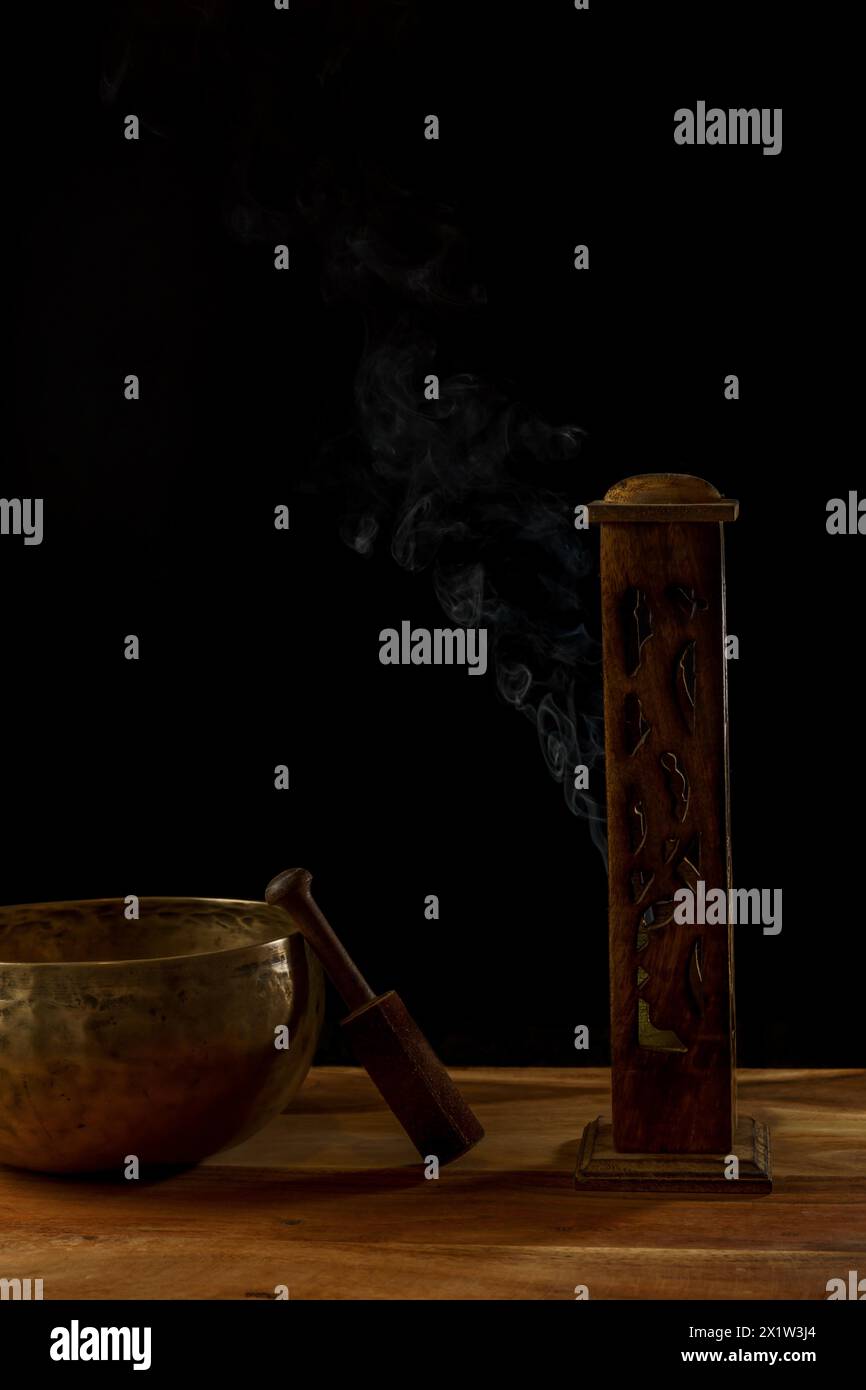 Bol chantant tibétain à côté d'une censure en bois avec de la fumée sortant isolé sur fond noir avec espace de copie Banque D'Images
