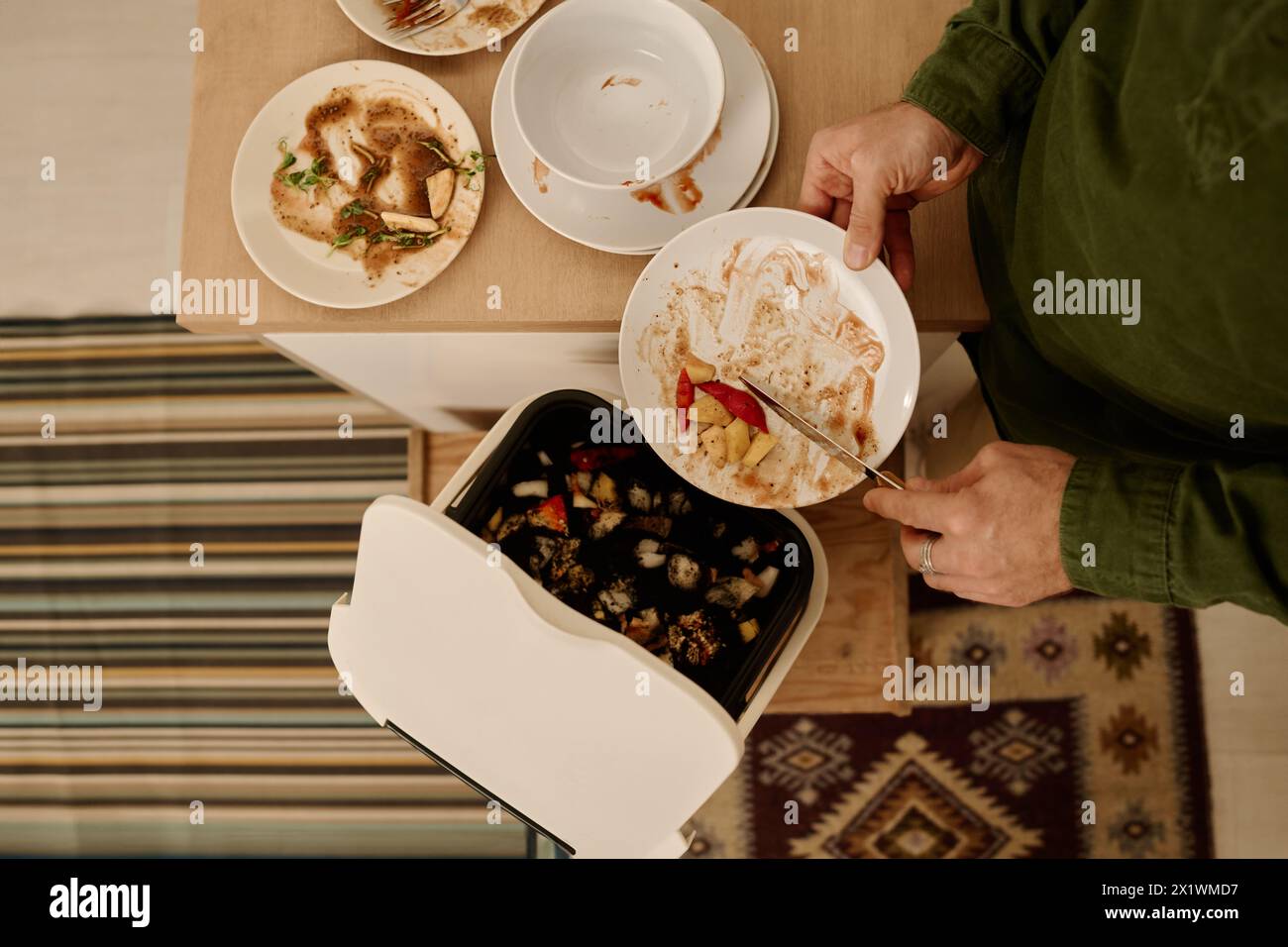 Vue de dessus des mains d'un jeune homme méconnaissable avec assiette jetant des restes de repas dans un seau en plastique ou une poubelle contenant de la terre Banque D'Images