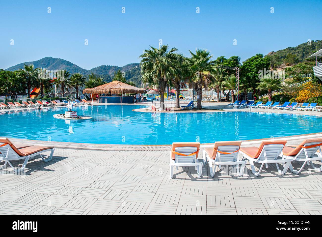 Piscine circulaire entourée de chaises longues et d'un bar avec toit de chaume, dans un parc aquatique d'été tôt le matin Banque D'Images
