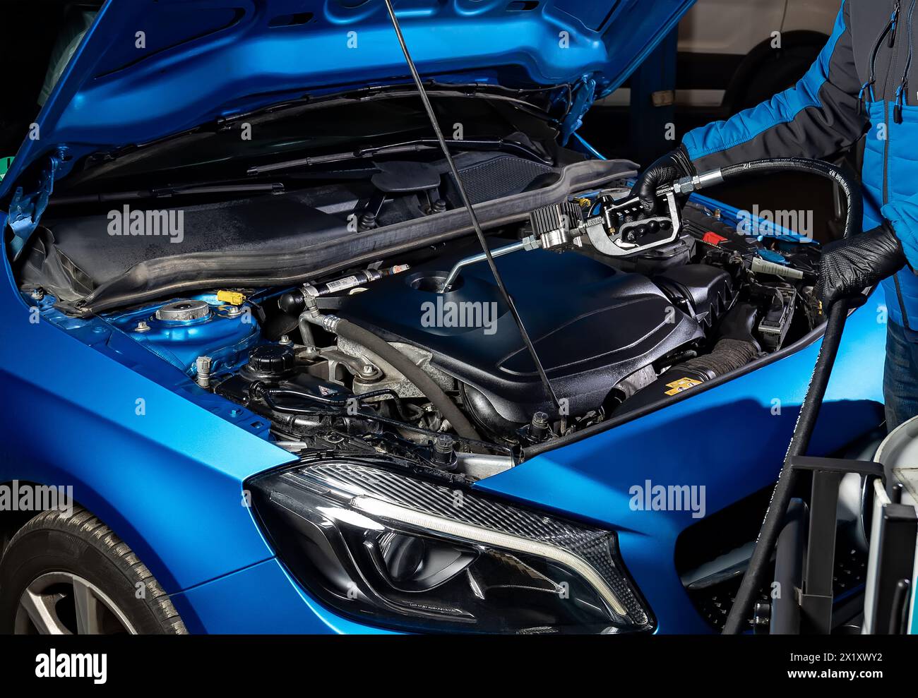 Entretien automobile en action comme un mécanicien remplit le moteur d'une voiture bleue avec de l'huile fraîche à travers un capot ouvert à l'aide d'une pompe à huile après avoir vidangé le Banque D'Images