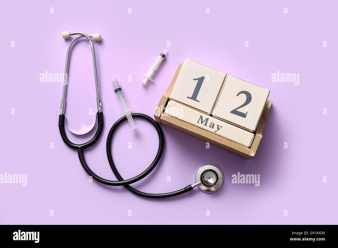 Calendrier avec stéthoscope et seringues sur fond lilas. Journée internationale des infirmières Banque D'Images