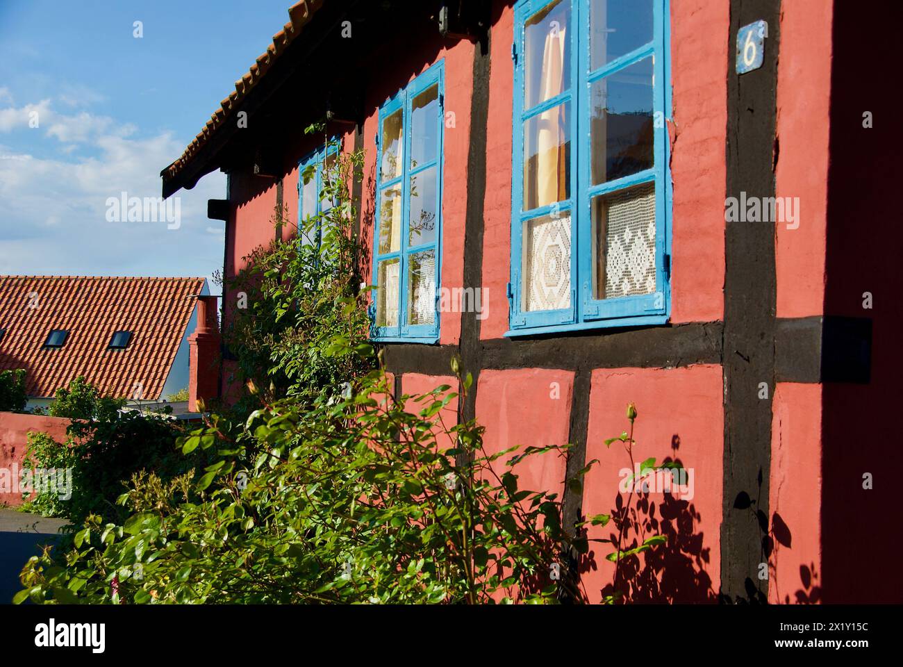 Extérieur d'un bâtiment rouge à colombages avec des fenêtres avec des cadres bleus et un jardin intérieur luxuriant. Banque D'Images