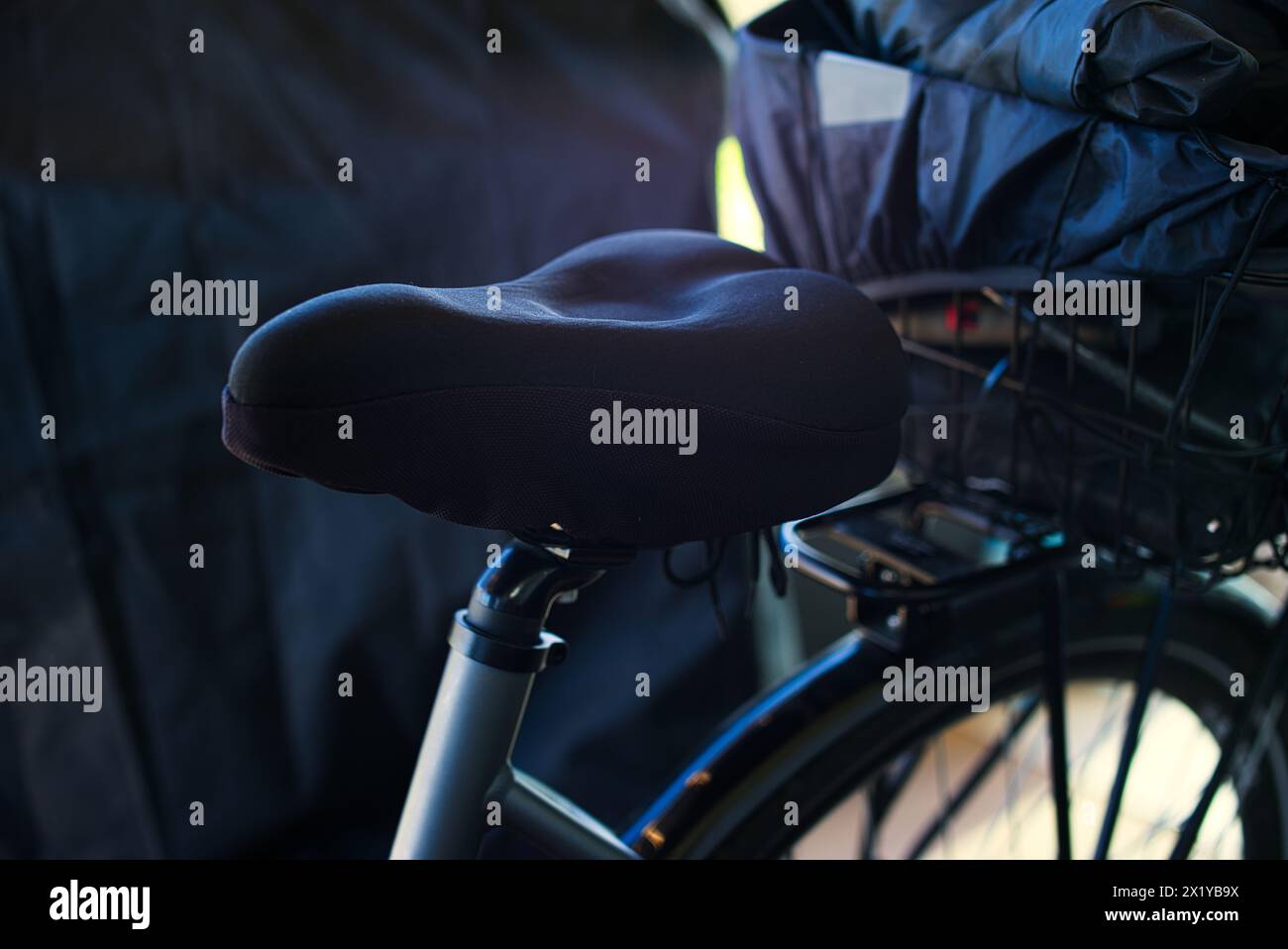 Siège de vélo rembourré noir avec une toile de fond de bâche noire. L'image montre une section du porte-bagages avec des accessoires de vélo sombres. Banque D'Images