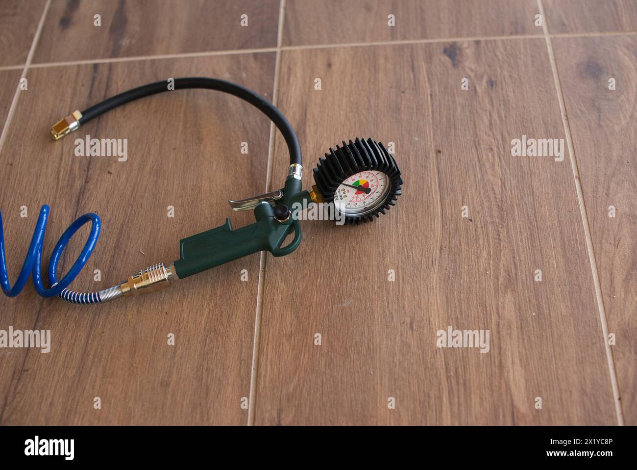 Manomètre avec une poignée verte, relié à un tuyau enroulé bleu, reposant sur des carreaux de sol en bois. Banque D'Images