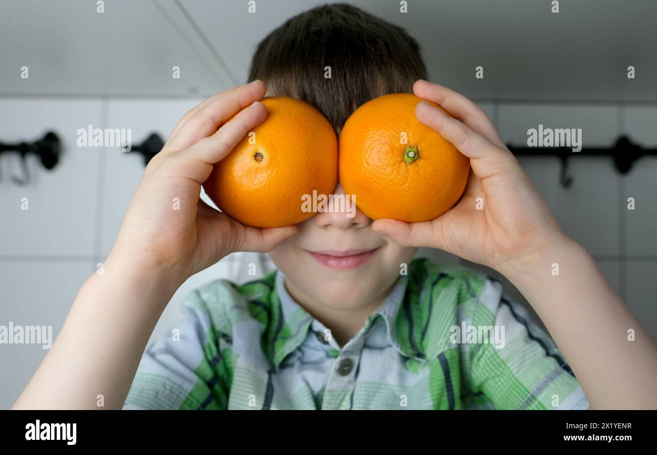 enfant, enfant 8-10, garçon assis dans la cuisine à la maison, oranges jaunes juteuses au lieu des yeux, gros plan de la tête, concept de régime alimentaire pour enfants, nourriture saine Banque D'Images