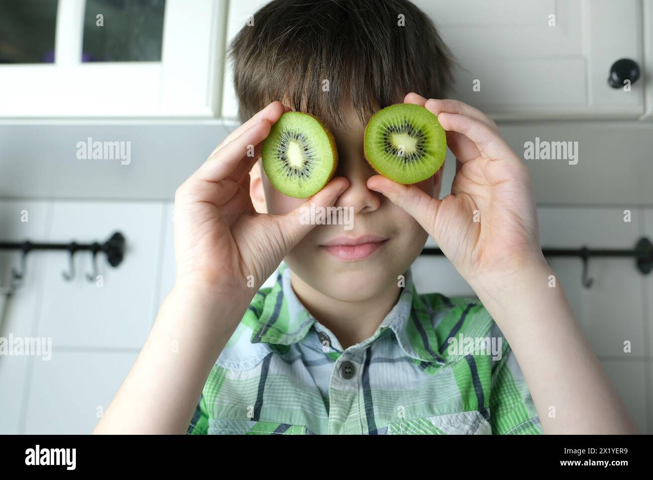 enfant, enfant 8-10, garçon assis dans la cuisine à la maison, kiwi vert coupé juteux au lieu des yeux, gros plan de la tête, concept de régime pour enfants, nourriture saine Banque D'Images