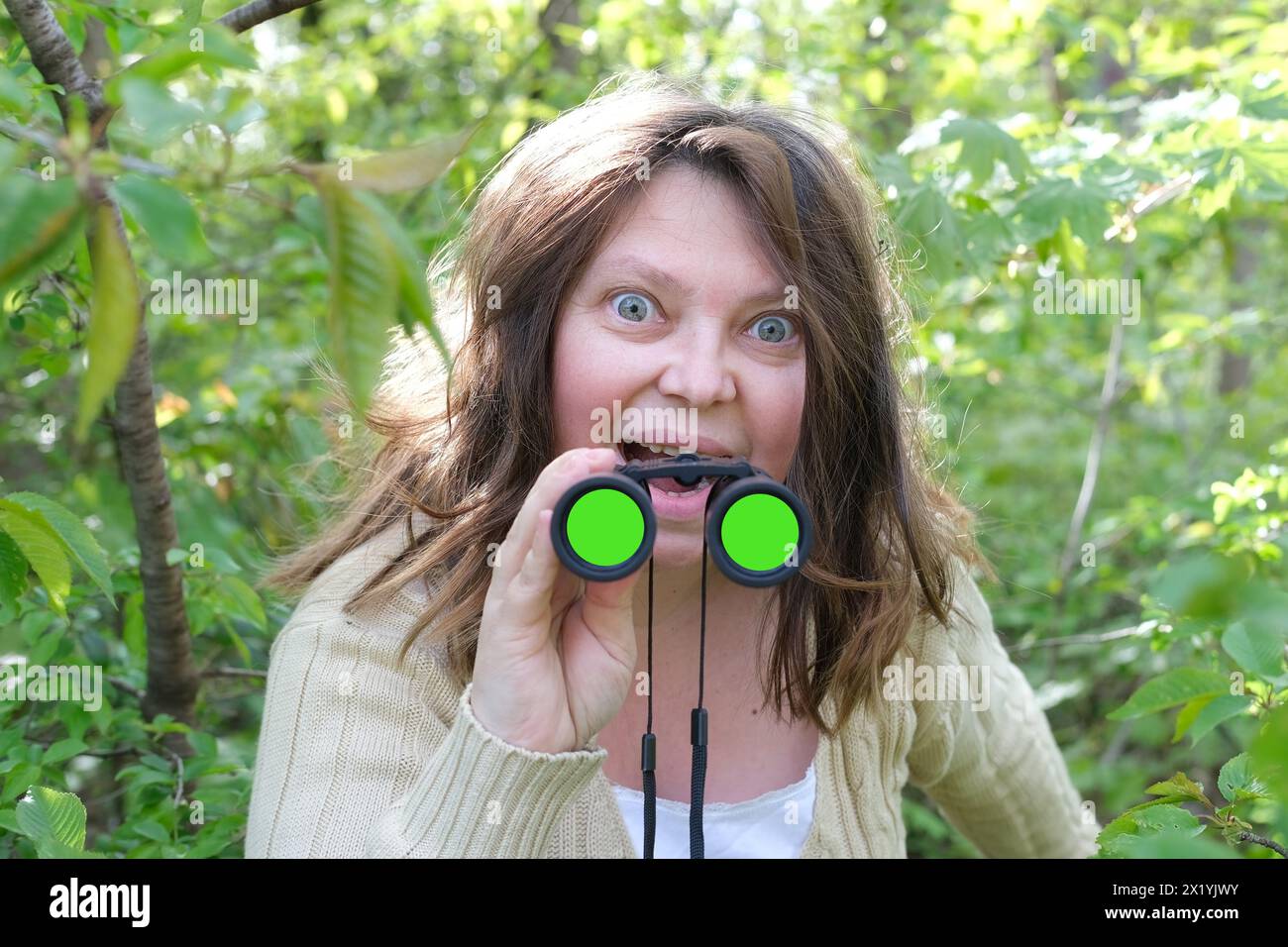 folle curieuse femme adulte européenne gros plan, tenant des jumelles à champ noir avec zoom, se cachant dans la verdure, regardant dans les buissons verts, espionnant l'infait Banque D'Images