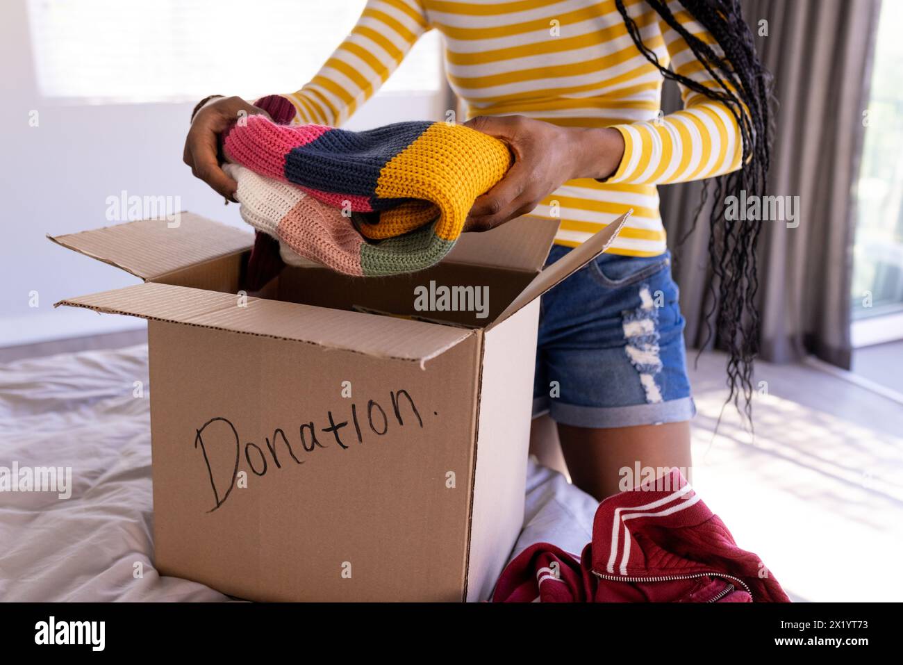 Une jeune femme afro-américaine est à la maison emballant des vêtements dans une boîte de dons Banque D'Images